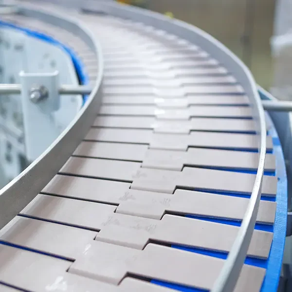 Curved conveyor belt in an industrial production line, showing interlocking belt tiles and metal guide rails on either side.
